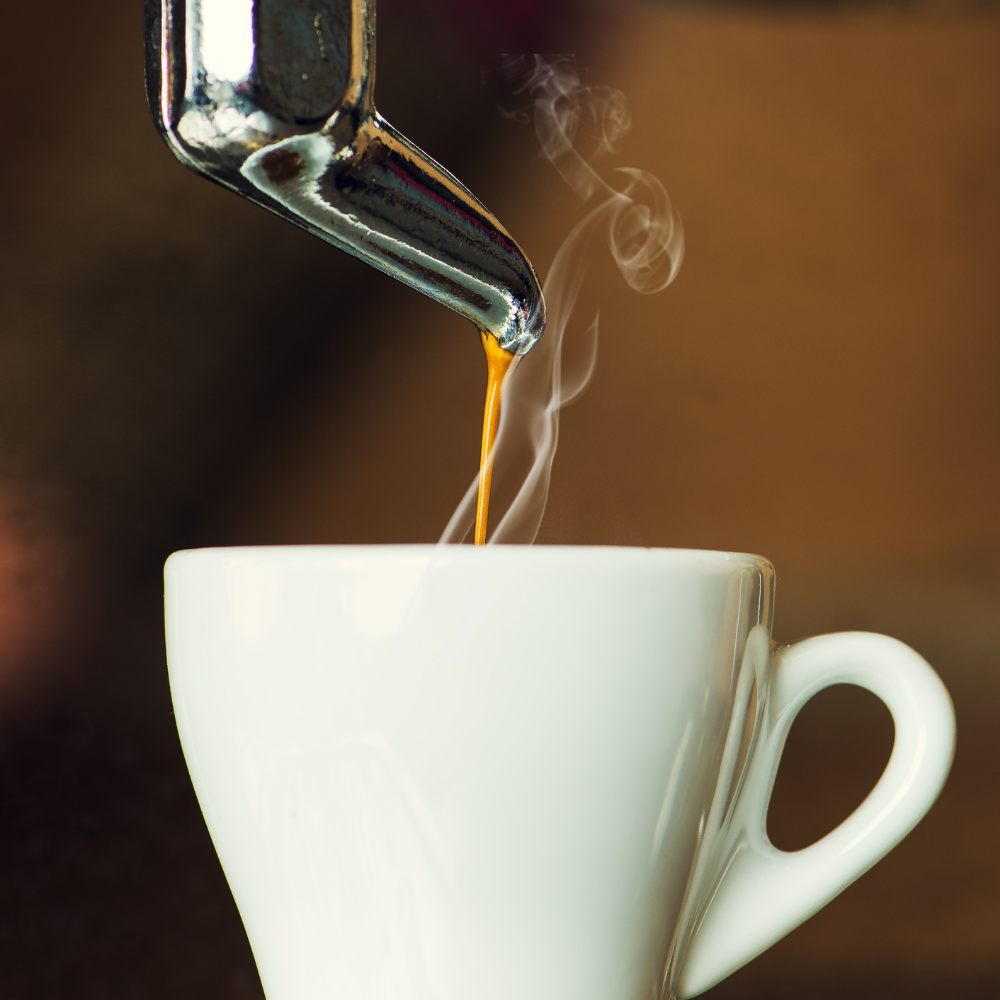Eine Kaffeetasse unter einem Siebträger auslauft, welche gerade gefüllt wird mit Kaffee und dieser dampft. 